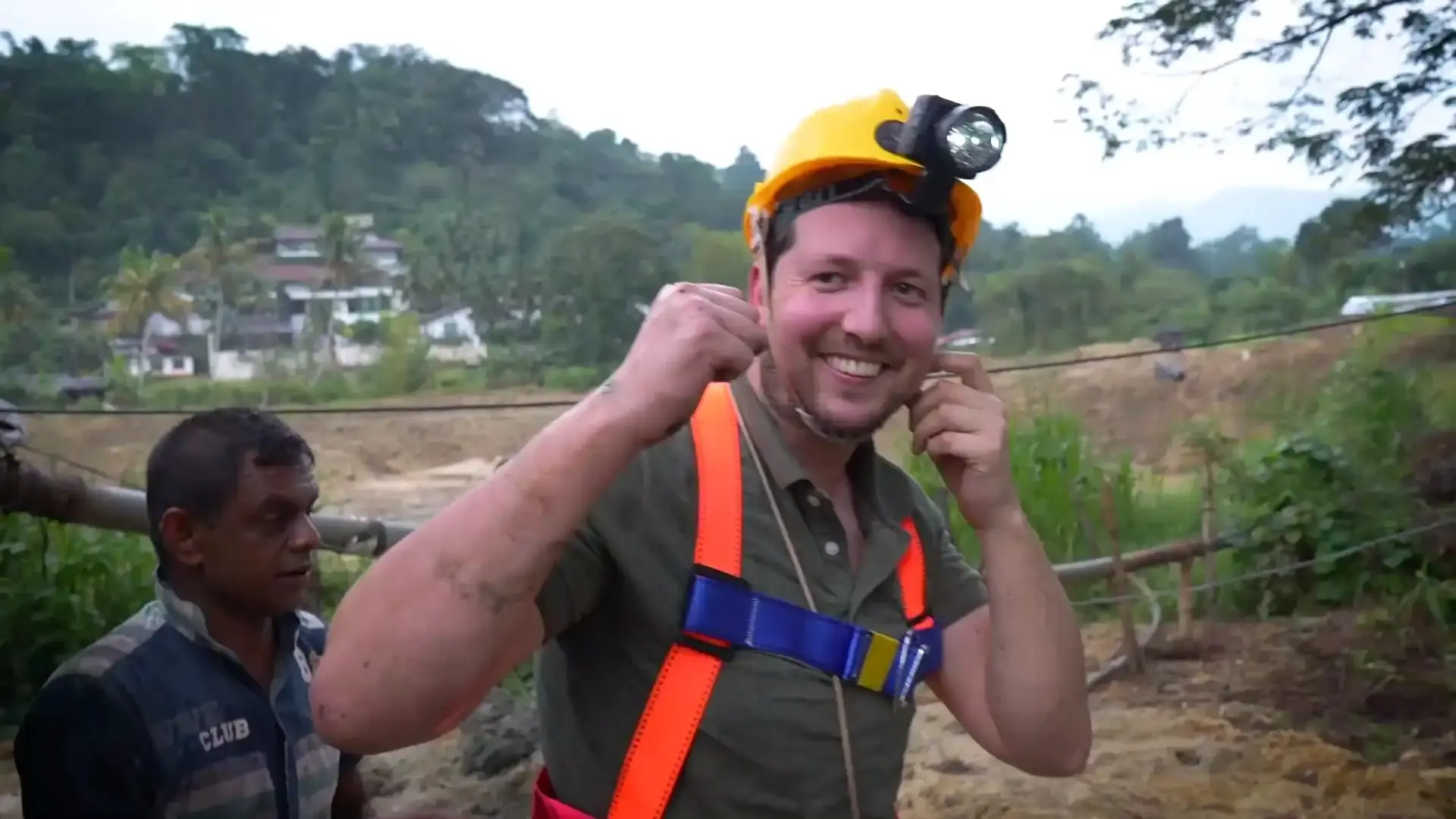 A happy tourist smiles while holding his helmet straps during a gem mine tour.