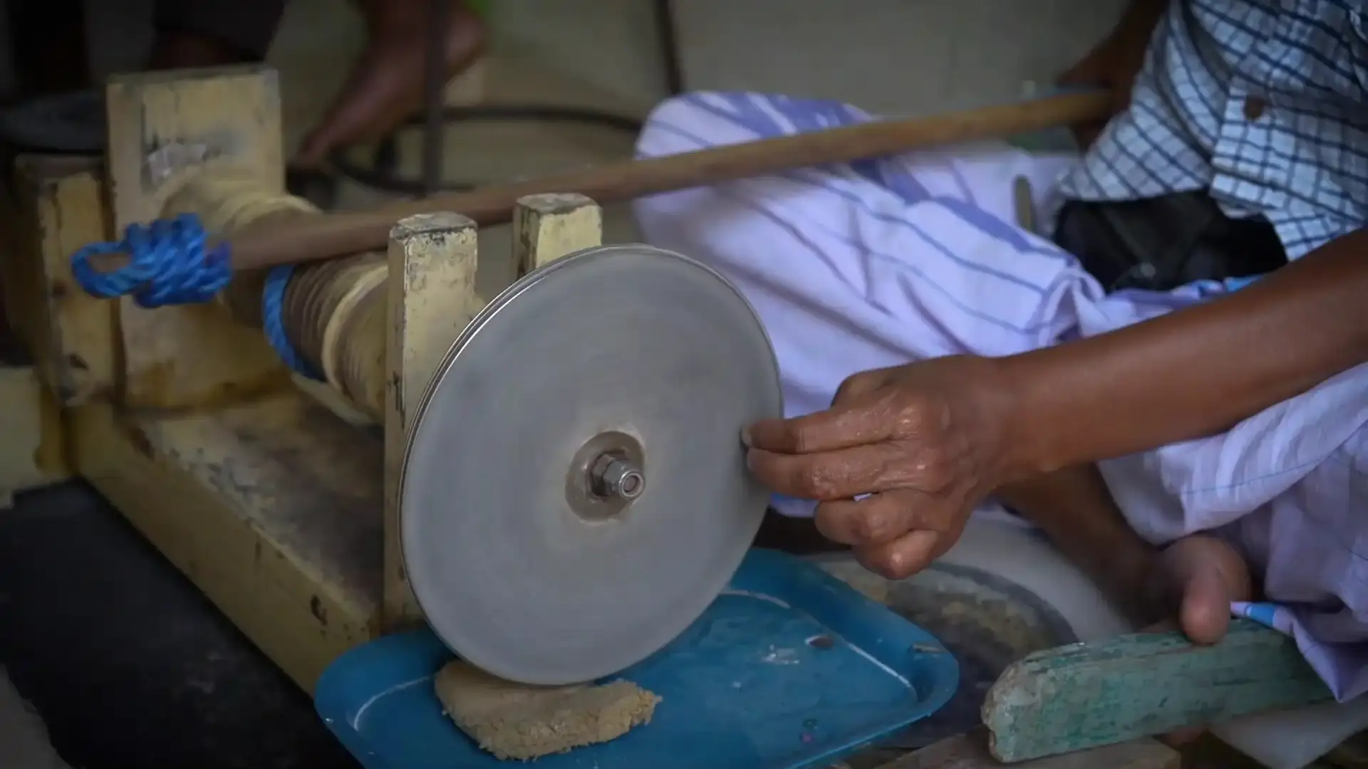 A person sharpens a tool on a traditional gem cutting wheel.